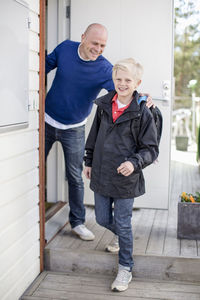 Portrait of happy boy leaving for school while father looking at him