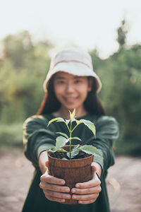 Portrait of man holding hat against plants