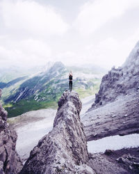 Man standing on rock by mountains against sky