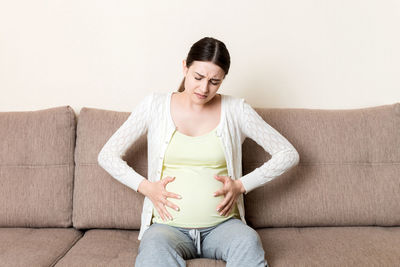 Pregnant woman with painful belly on sofa at home.