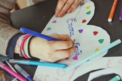 Cropped hand of girl writing on heart shape paper at home
