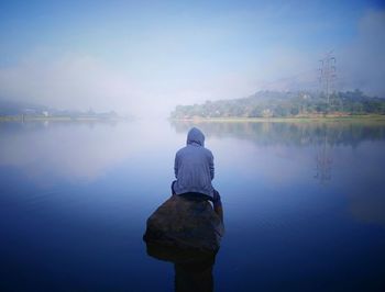 Rear view of man standing on lake against sky