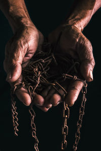 Cropped hands of man holding chain against black background