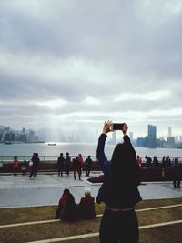 Rear view of man photographing woman on city against sky