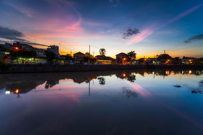 Reflection of illuminated buildings in lake against sky during sunset