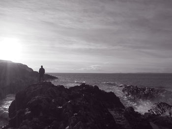 Silhouette man standing on cliff by sea against sky