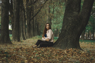 Young woman sitting on tree trunk in forest