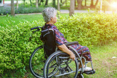 Full length side view of senior woman sitting on wheelchair in park