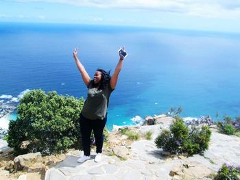 High angle view of happy woman gesturing while standing on rocks against sea