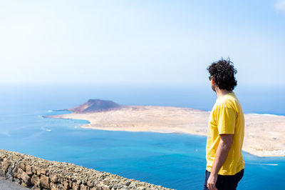 Rear view of woman standing at beach against clear sky