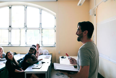 Happy teacher holding book and felt tip pen while teaching language to students