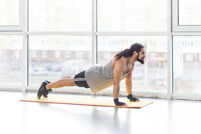 Side view of young exercising by window