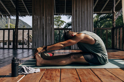 Side view of man doing stretching while sitting on exercise mat at wellness resort
