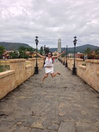 Woman jumping on street against cloudy sky