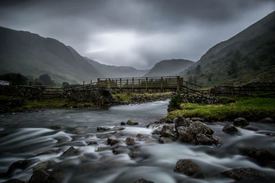 Scenic view of river flowing by mountains against sky