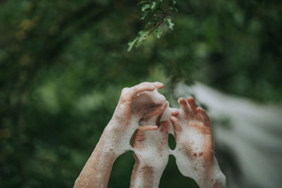 Cropped hands of people with soap sud against trees
