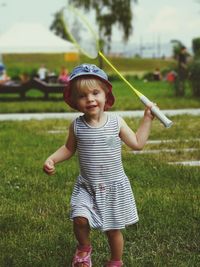 Portrait of cute girl holding badminton racket while walking on grass