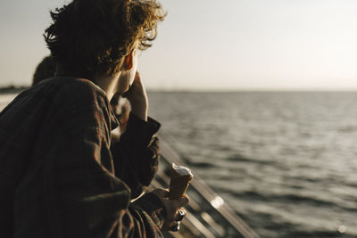 Teenage boy holding ice cream cone while looking at sea