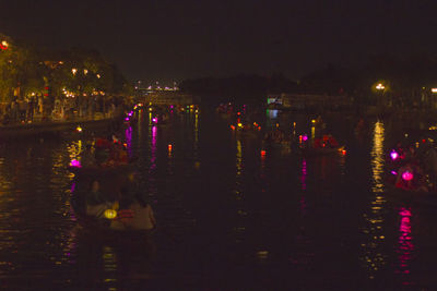 Illuminated city by river against sky at night