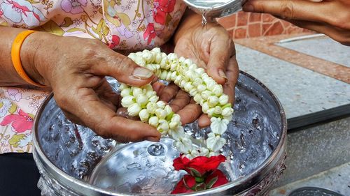 Midsection of woman washing flowers necklace in bowl