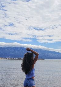 Rear view of woman standing at beach against cloudy sky