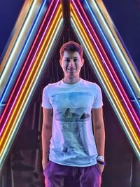 Portrait of young man standing against illuminated light trails rainbow