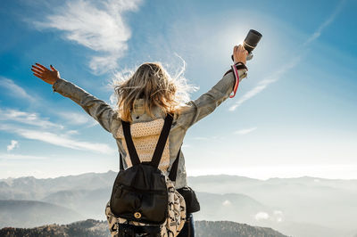 Woman with arms outstretched standing on mountain against sky