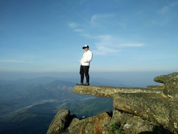 Side view of man sitting on cliff against sky