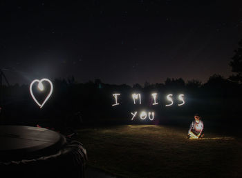 Man sitting on field by illuminated text at night