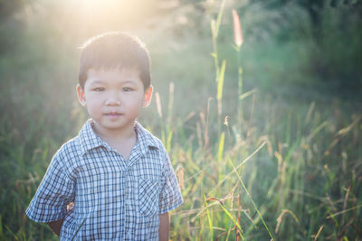 Portrait of cute boy standing on grassy field during sunny day