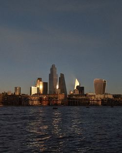 Sea by illuminated city against clear sky