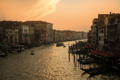 Boats in canal amidst cityscape against sky during sunset