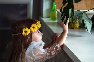 Rear view of small girl with leaves of pot plant at home