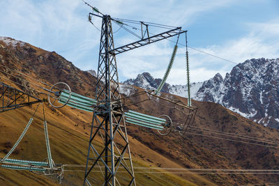 Electricity pylon by snowcapped mountains against sky