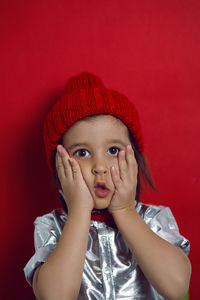 Boy child in a red knitted hat on the background in the studio surprised
