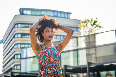 Fashionable young woman with curly hair looking away in city