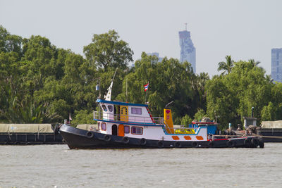 Boats in river by trees against sky