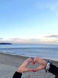 Woman making heart shape with fingers against beach