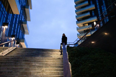 Low angle view of woman sitting by steps on railing against sky at dusk