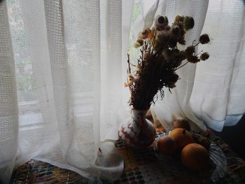 Flower pot with flowers and bowl of pumpkin by closed curtain