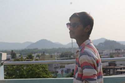 Young man standing against railing on building terrace