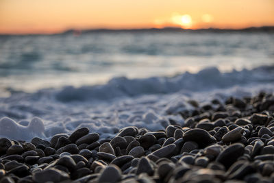 Surface level of rocks at beach against sky during sunset