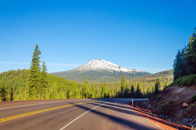 Empty road with snowcapped mt bachelor in background against blue sky