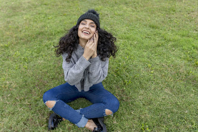 High angle view of happy young woman talking over smart phone while sitting on land