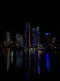 Illuminated buildings by river against sky at night