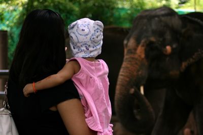 Rear view of mother with baby girl standing by elephant