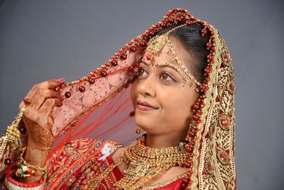 Close-up of smiling bride in traditional clothing over gray background