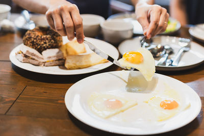 Woman eating fried eggs breakfast with friends on wooden table.