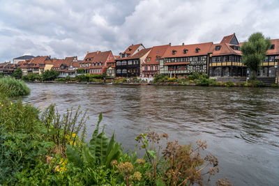 View of buildings by river against cloudy sky