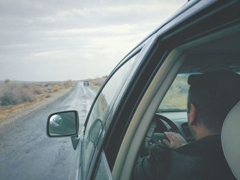 Close-up of man driving car on road against sky